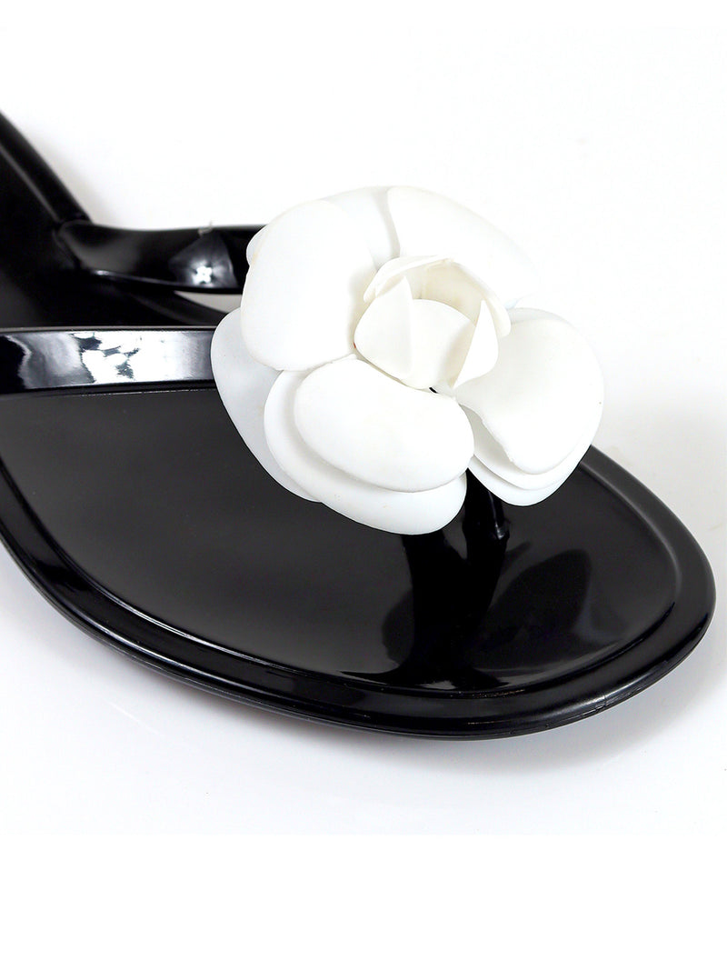 A close-up of Frederick's of Hollywood Jelli Camellia Thong Sandals in black with a glossy finish and a bold white flower on the strap‚Äîstylish, feminine footwear ideal for warm weather.