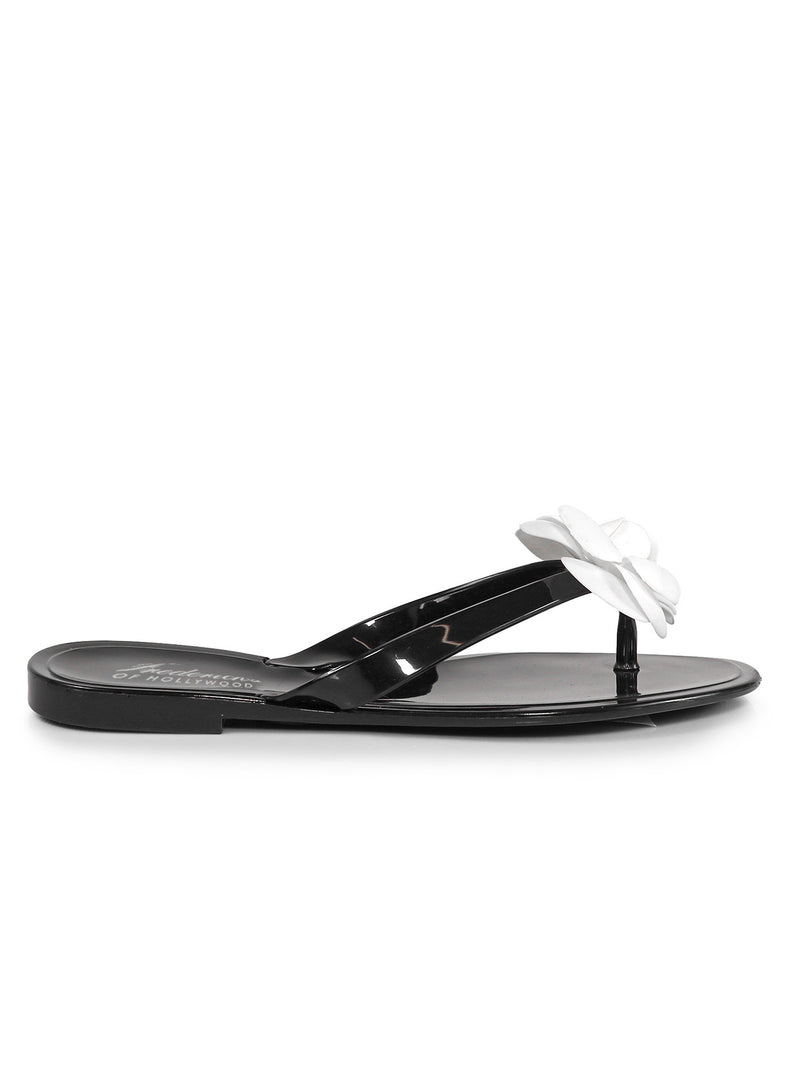 The Jelli Camellia Thong Sandals by Frederick's of Hollywood feature a black glossy finish and a white flower on the strap, shown in side profile against a white background‚Äîideal feminine footwear for warm weather.