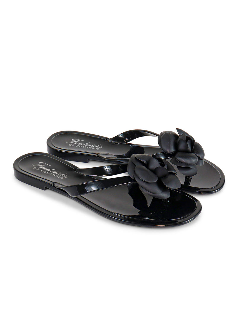 The Frederick's of Hollywood Jelli Camellia Thong Sandals feature glossy black finish and floral strap embellishments, perfect for warm-weather outfits. Photographed on a white background.