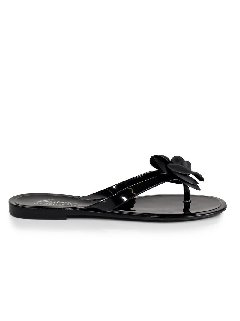 The Frederick's of Hollywood Jelli Camellia Thong Sandals feature a shiny black finish, flat sole, and 3D flower on the strap‚Äîideal for warm-weather looks. Shown in side view against a white background.