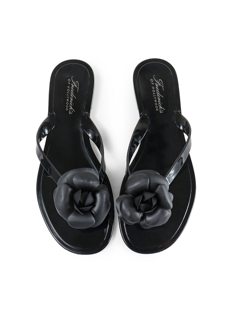 A pair of glossy black Jelli Camellia Thong Sandals by Frederick's of Hollywood, featuring large camellia-inspired flower accents on the straps, displayed on a white background.