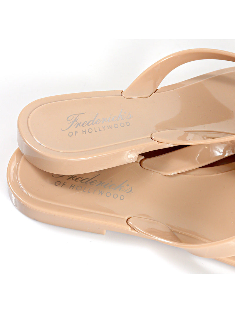 Close-up of two stacked beige Jelli Camellia Thong Sandals by Frederick's of Hollywood, featuring subtle camellia details and silver branding on the insole, set against a white background.