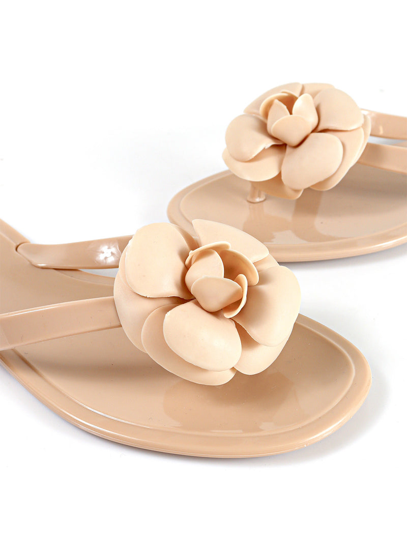 A close-up of beige Jelli Camellia Thong Sandals by Frederick's of Hollywood, showcasing large camellia accents on the straps, set against a white background.