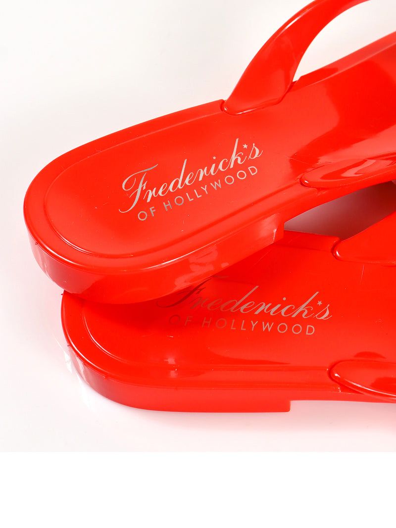 Close-up of two vibrant red Jelli Camellia Thong Sandals stacked together, showcasing camellia-inspired details and the Frederick's of Hollywood logo in white script on the insole.