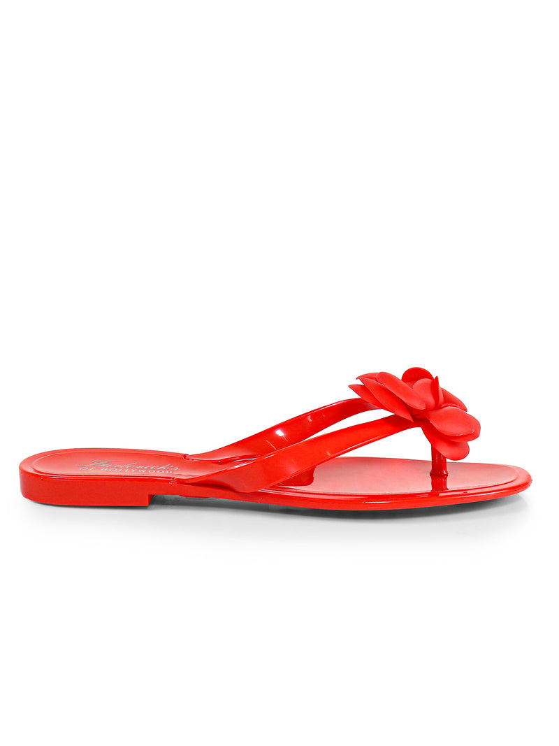 The Jelli Camellia Thong Sandals by Frederick's of Hollywood are bright red flats with a flower detail on the strap, shown in side view against a white background‚Äîstylish and ideal for warm weather.