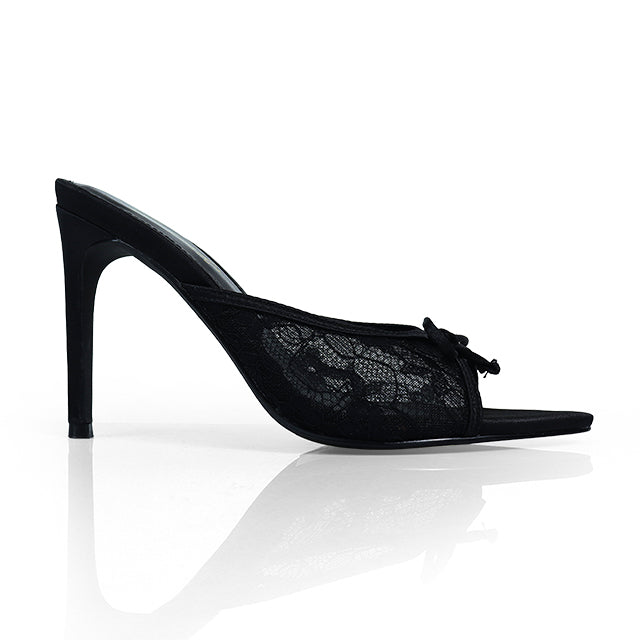 The Lacey Pointed Toe Lace Bow Heels by Frederick's of Hollywood feature black lace sides and a stylish bow, captured on a white reflective surface.