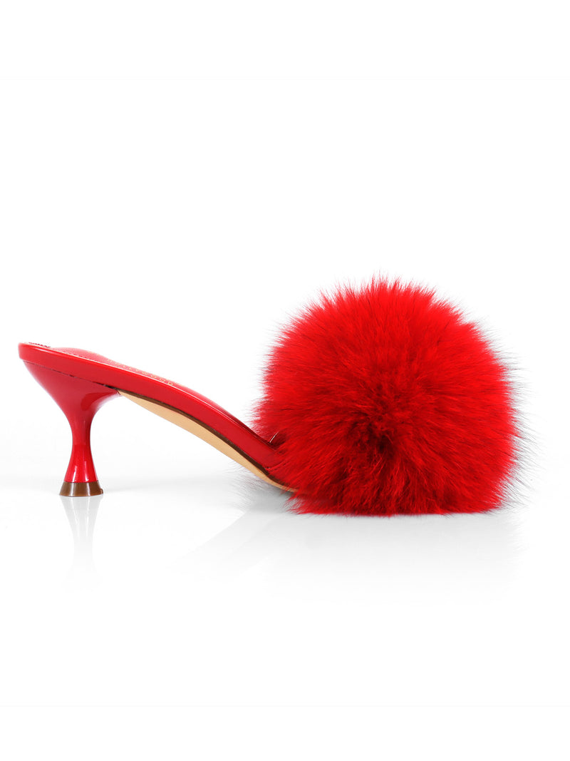 The Frederick’s of Hollywood Purr Square Toe Fur Heel is a red mule shoe with a chic square-toe silhouette, a mid-height heel, and a large fluffy red pom-pom adorning the upper front, displayed on a white background.