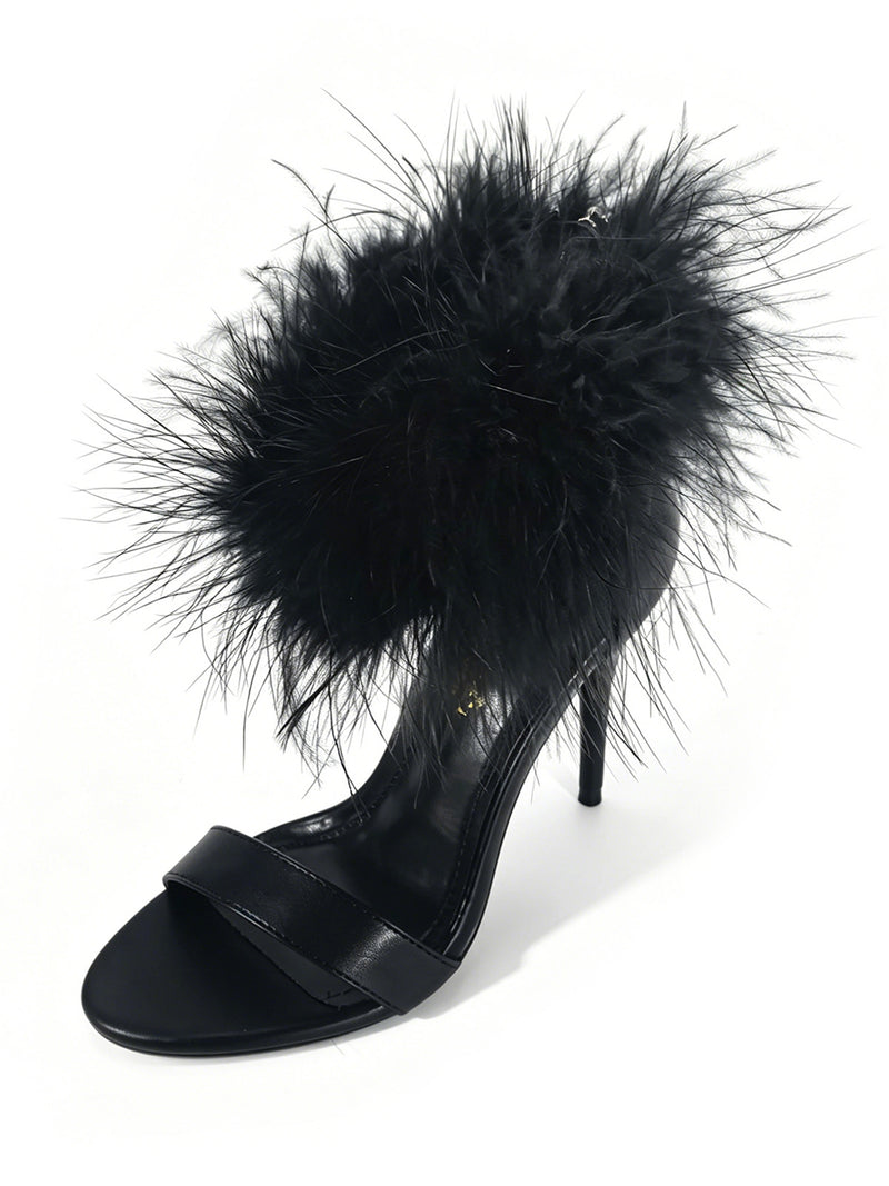 The Raquel Feather Stiletto Heel by Frederick’s of Hollywood is a black high-heeled sandal featuring a fluffy, feathery black strap across the ankle and an open toe design. This modern luxury shoe showcases a sleek stiletto silhouette against a crisp white background.