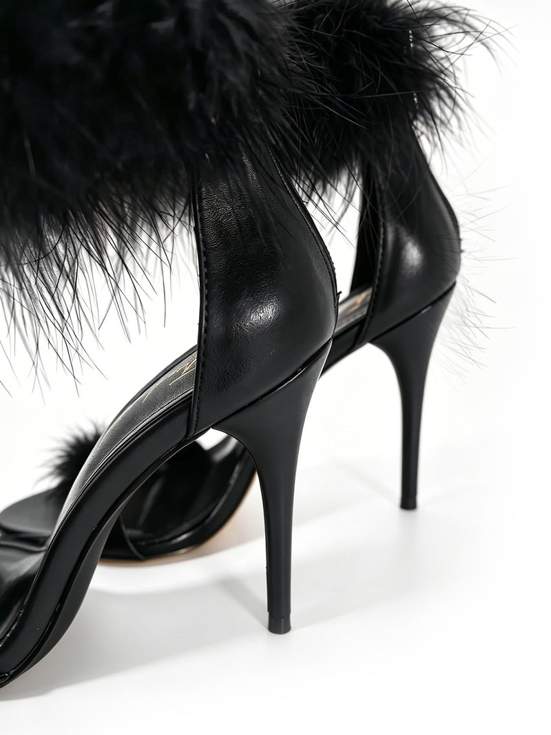 Close-up of the Raquel Feather Stiletto Heel by Frederick’s of Hollywood, featuring a bold black stiletto silhouette and elegant black feather detailing on the ankle straps, embodying modern luxury, shown on a white background.