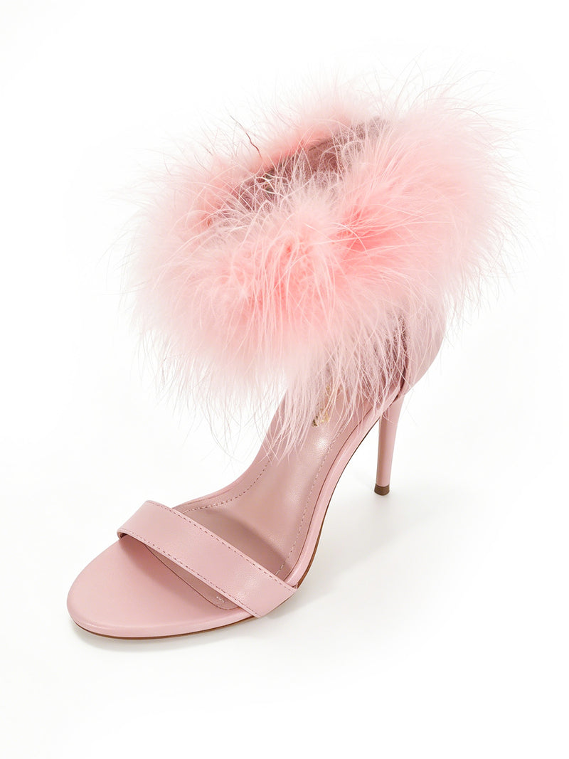 Introducing the Raquel Feather Stiletto Heel by Frederick’s of Hollywood: a chic pink sandal set against a white background, featuring a single toe strap and elegant feather detailing with fluffy, light pink trim around the ankle strap—an eye-catching statement piece for any bold look.
