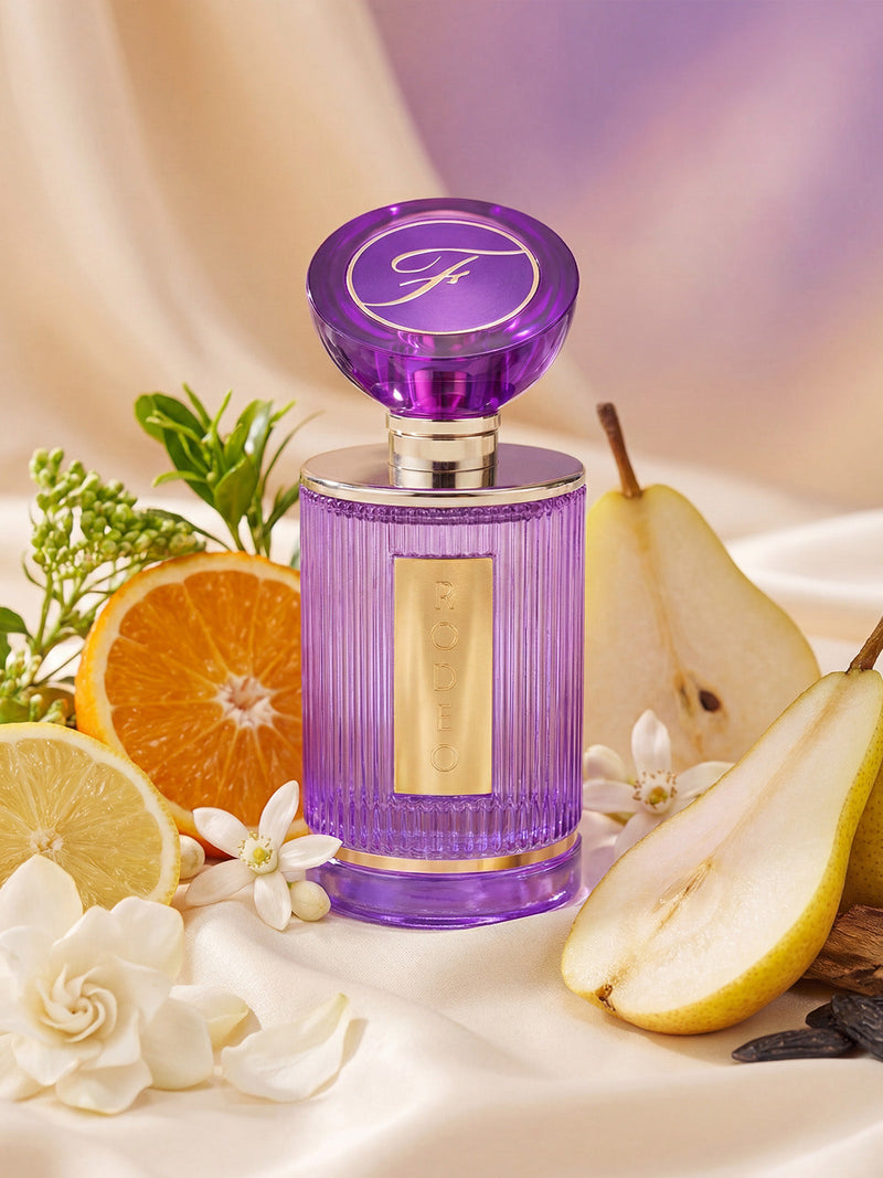 Rodeo 60ml Eau De Parfum by Frederick's of Hollywood stands out in a pastel purple bottle with a gold label, surrounded by pear, lemon, orange, and white flowers on cream fabric—evoking its seductive citrus floral scent.