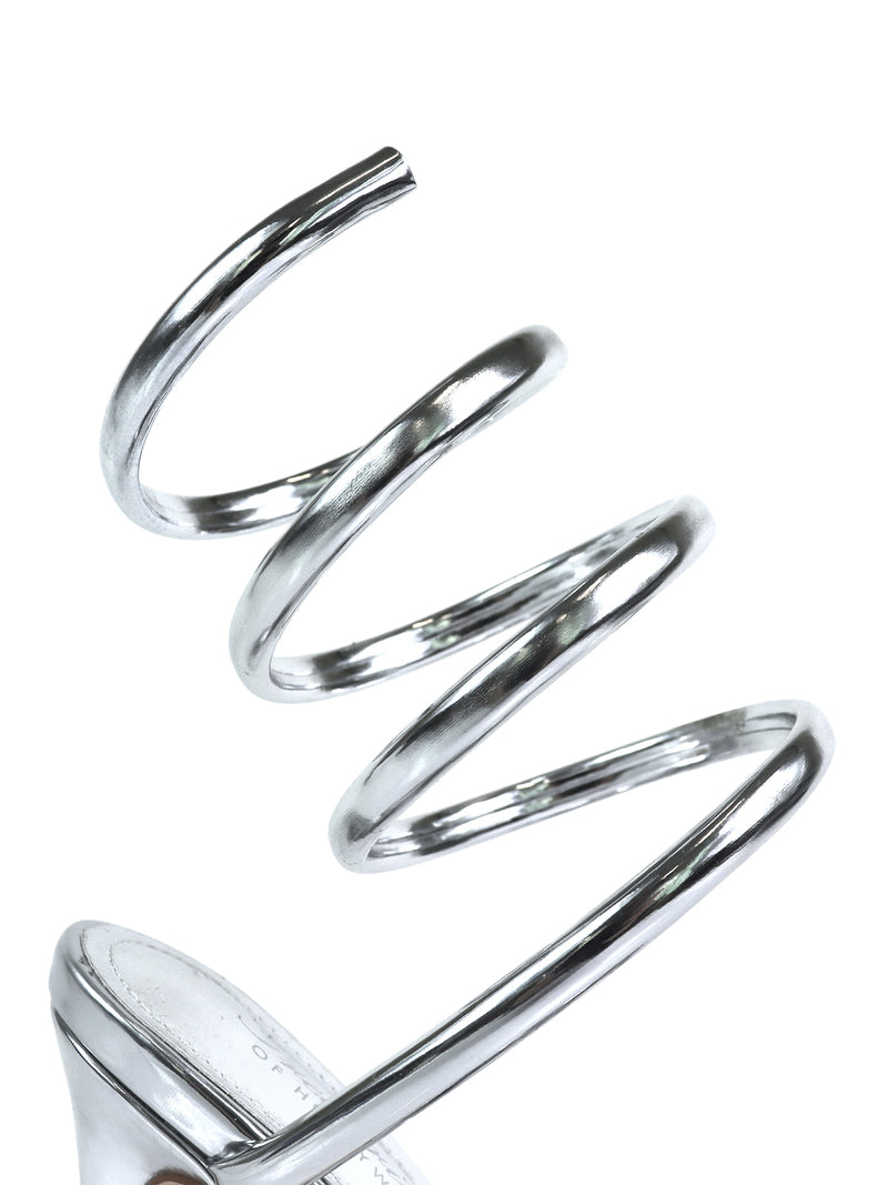 The Sabine Round Toe Heel by Frederick's of Hollywood features a shiny metallic silver spiral strap wrapping upward like a spring, with a round toe design for style and comfort. Shown against a white background.