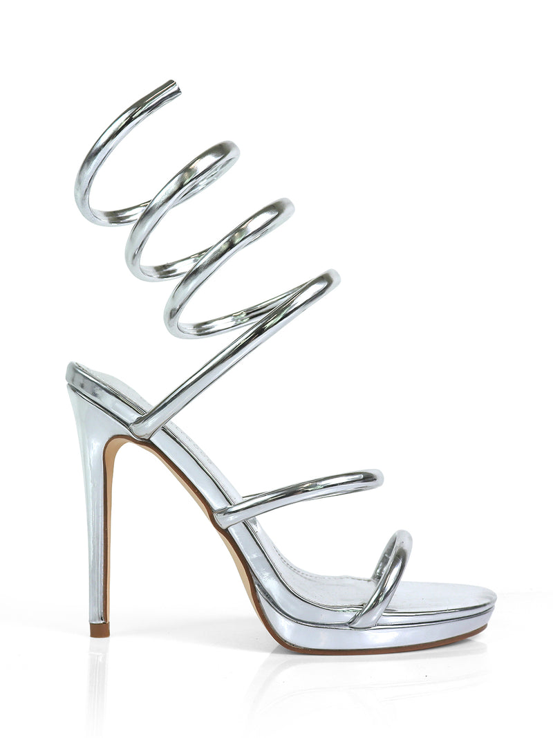 The Sabine Round Toe Heel by Frederick's of Hollywood is a metallic silver sandal with multiple spiral ankle straps, a thin stiletto heel, and an open toe for a modern, sculptural look.