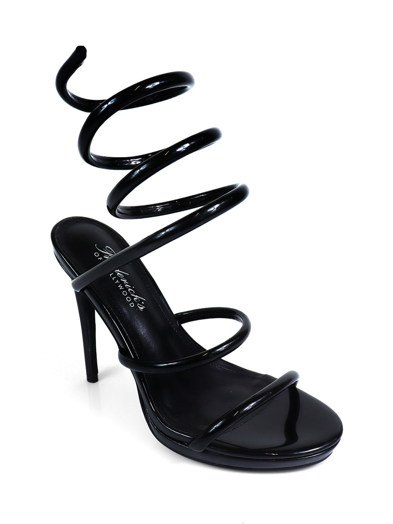 The Sabine Round Toe Heel by Frederick's of Hollywood is a black high-heeled sandal with thin straps and a distinctive spiral ankle strap that coils upward, offering a bold, sculptural look.