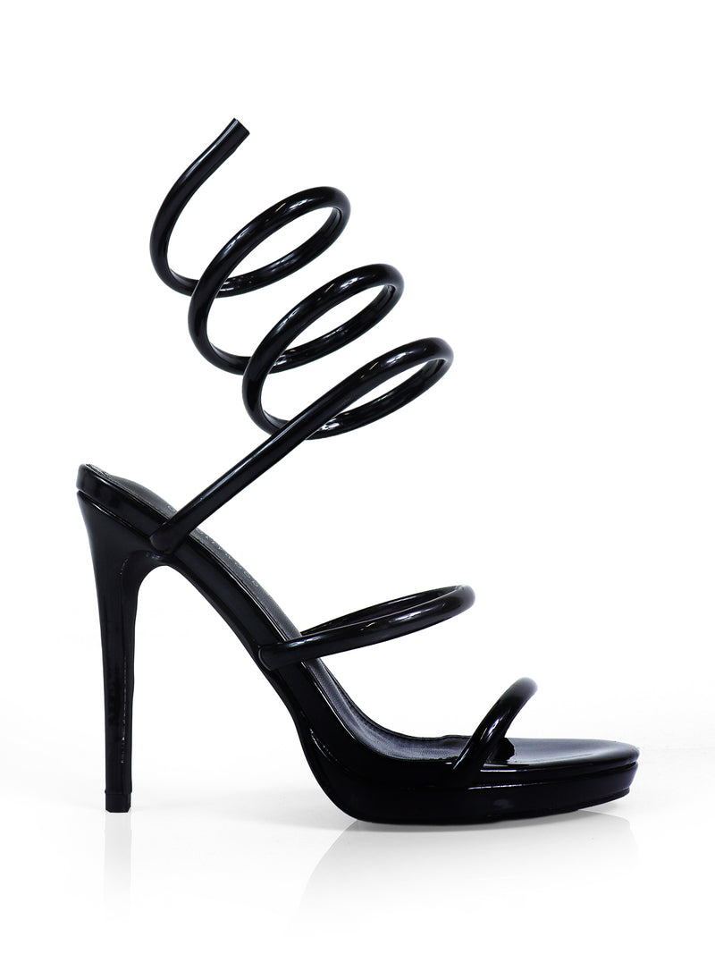 The Sabine Round Toe Heel by Frederick's of Hollywood is a black high-heeled sandal with a glossy finish, featuring unique spiral ankle straps and an open toe. These elegant stilettos are perfect for any occasion.