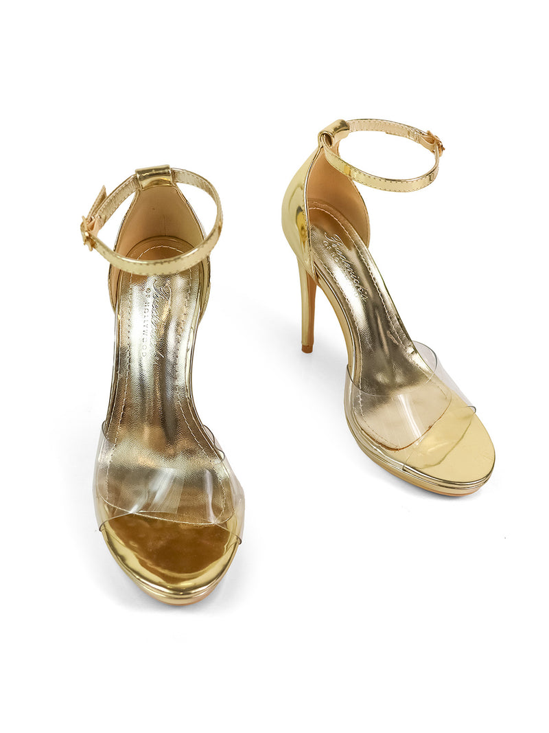 The Stacy Ankle Strap Heels by Frederick's of Hollywood are elegant gold high heels with clear straps and ankle buckles, showcased on a white background.