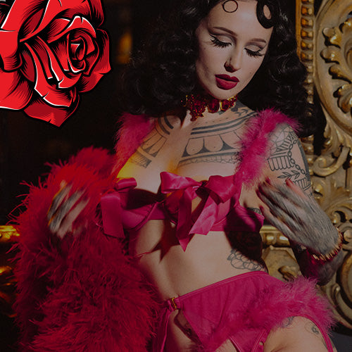Woman in a pink outfit with tattoos, surrounded by decorative elements including a red rose.