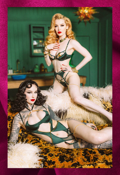 Two women in vintage-style lingerie posing in a room with green walls and decorative elements
