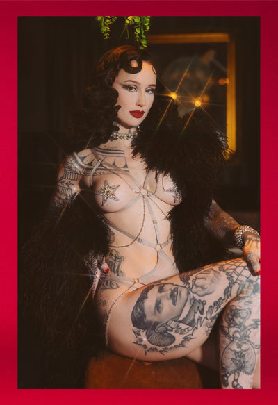 Person with tattoos in silver cutout lingerie teddy in a dark setting