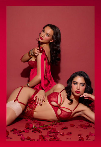 Two women in red lingerie posing on a red background with rose petals.