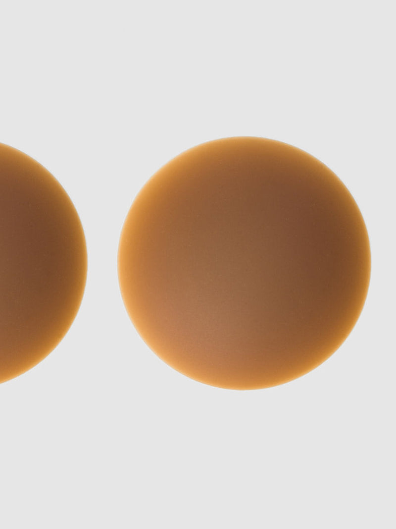 Close-up of Frederick's of Hollywood Silicone Nipple Covers—two round, skin-toned pads shown against a white background, with one full pad on the right and part of another on the left for seamless coverage.