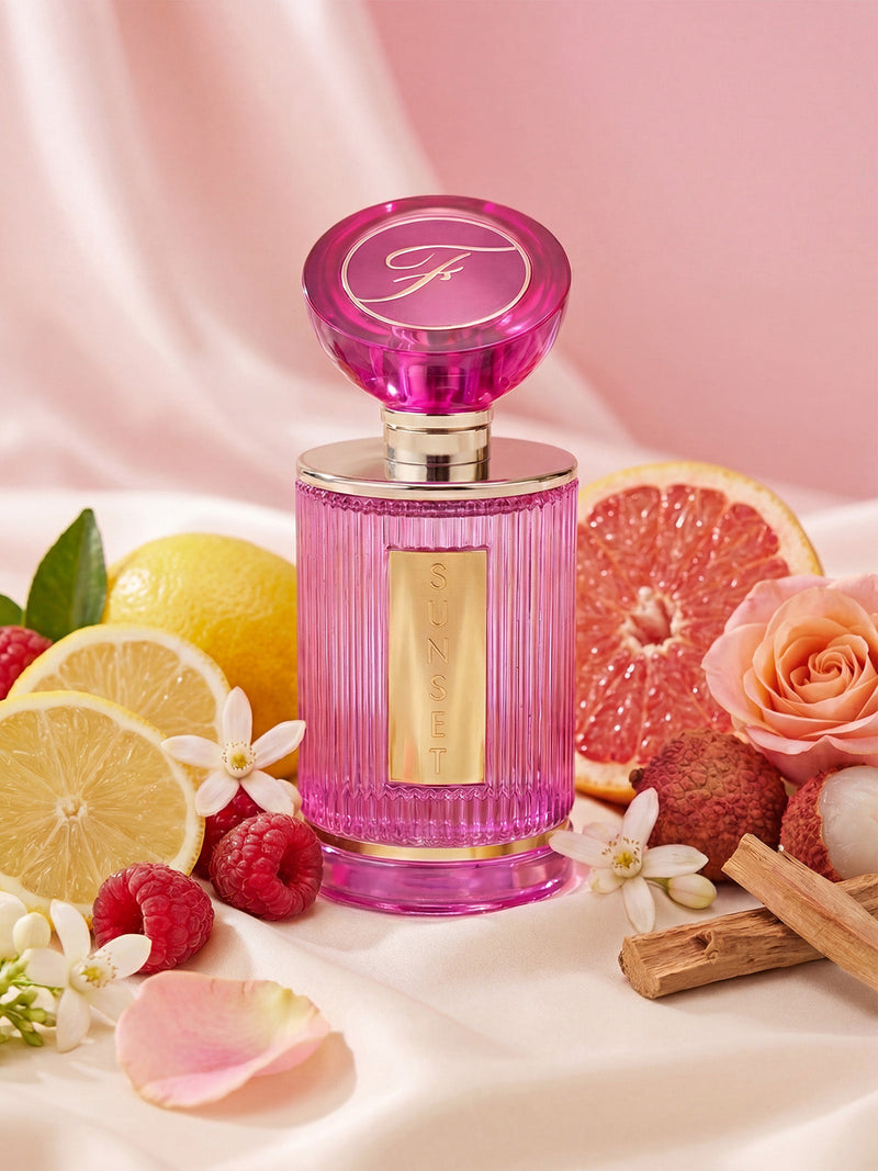 Frederick's of Hollywood Sunset 100ml Eau De Parfum, a warm evening scent, is showcased with grapefruit, lemon, raspberries, white flowers, cinnamon sticks, and rose petals on a soft pink backdrop.