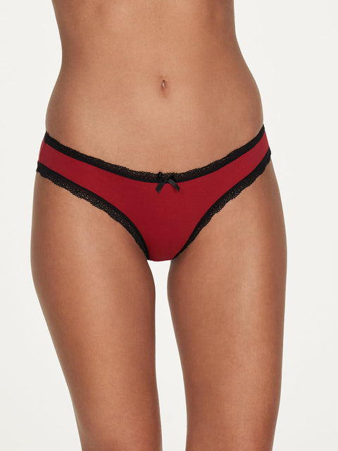 Model wears the Cora Cotton & Lace Hipster by Frederick's of Hollywood, featuring red cotton with black lace trim and a small black bow, shown from mid-torso to upper thighs against a plain light background.