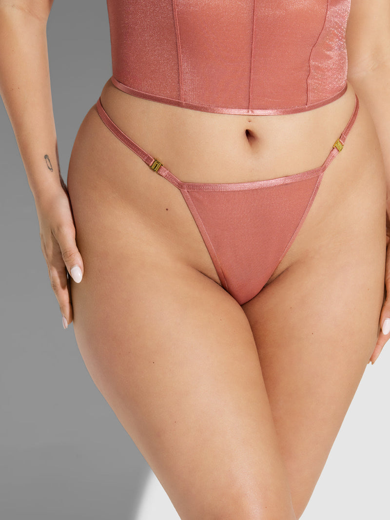 A person wears the Frederick's of Hollywood Pia Mesh G-String—shimmery pink with an embossed waistband—paired with a matching crop top, standing against a neutral background with one hand on their hip.