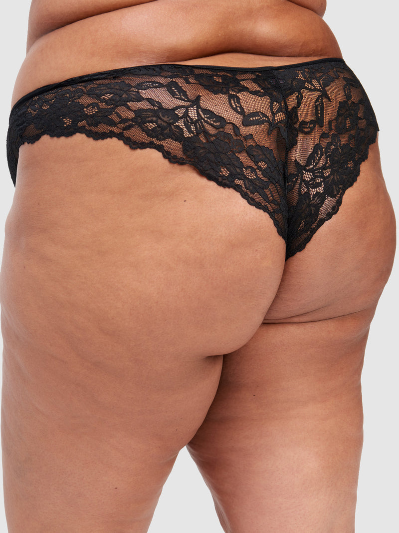 A close-up of a person wearing the Frederick's of Hollywood Mabel Lace Up Front Tanga, featuring black stretch lace with a scalloped floral pattern, shown from the back against a neutral background.