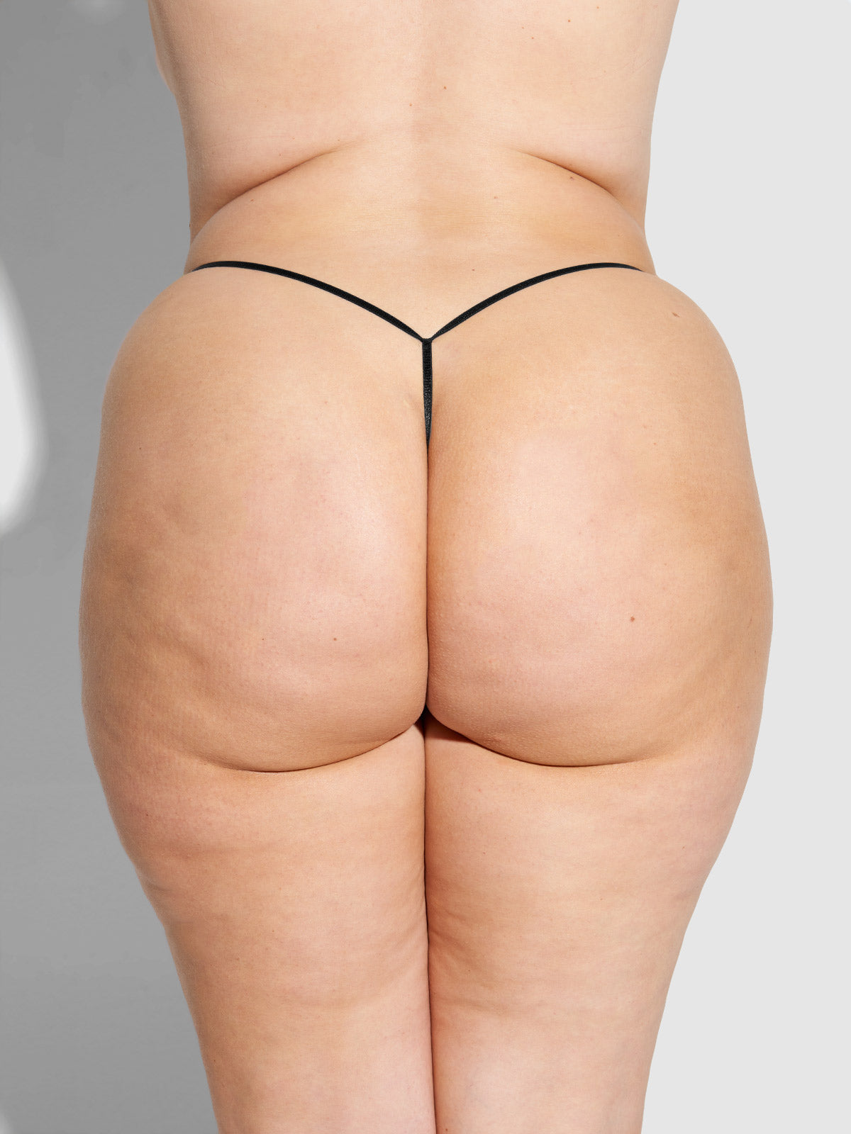 A person shown from the waist down wears the Frederick’s of Hollywood Lexi Liquid Satin G-String, highlighting visible skin texture and cellulite against a plain light background.