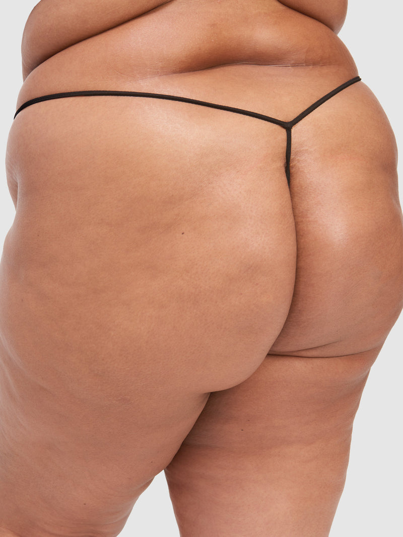A close-up of a person wearing the Mabel Lace G-String by Frederick's of Hollywood, highlighting their lower back, buttocks, and upper thigh with visible skin texture and natural feminine curves.