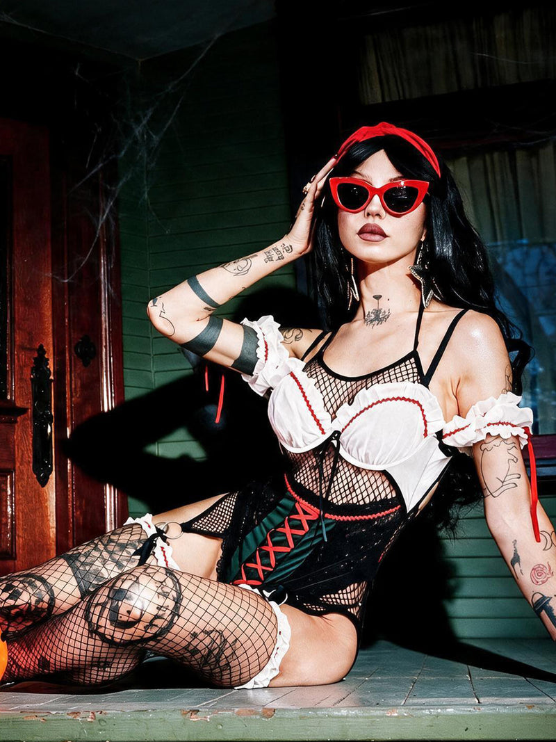 A person poses confidently indoors wearing the Frederick’s of Hollywood Biergarten Babe Crotchless Teddy With Detachable Garters, paired with a corset and red sunglasses. They have long dark hair, tattoos, and complete the look with a red headband featuring a bow, giving off a modern Snow White vibe.