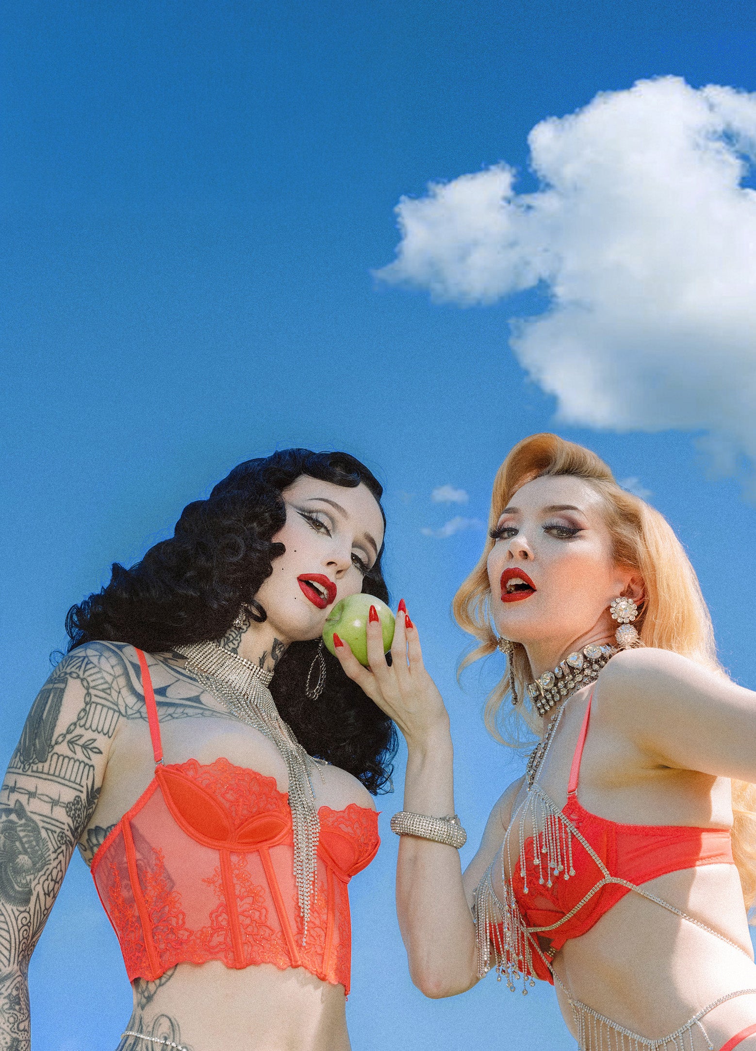 Two women in red bikinis against a blue sky with white clouds.
