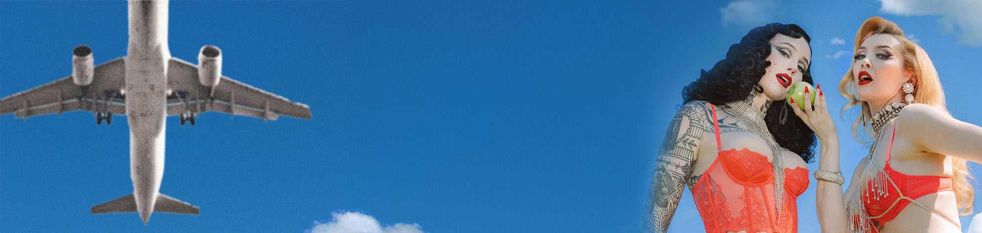 Two women in red dresses standing next to an airplane against a blue sky.