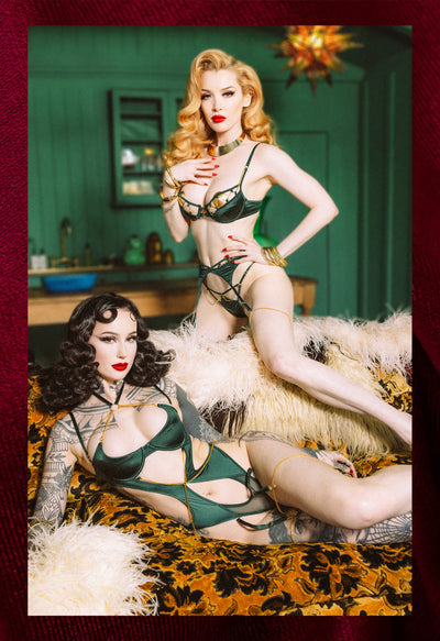 Two women in vintage-style lingerie posing in a room with green walls and decorative elements.