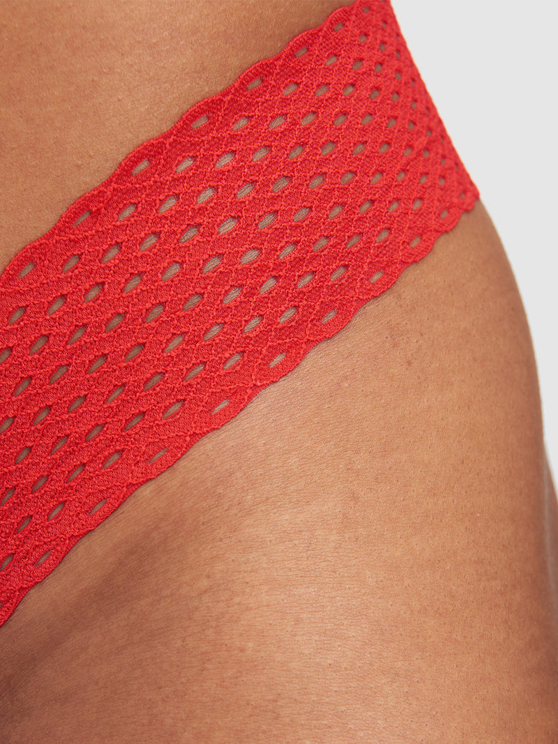 Close-up of a person's hip wearing the Abby Rose Mesh Thong by Frederick's of Hollywood, featuring red mesh and lace trim for playful sex appeal and bold style against a plain background.
